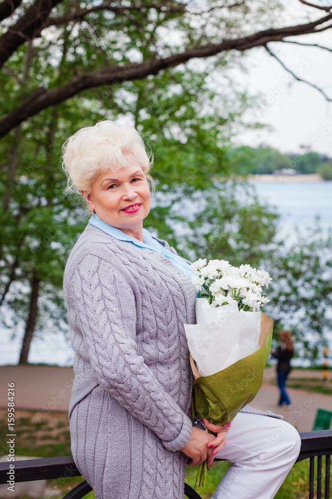 old woman standing in a park with a bouquet of flowers old woman standing in a park with a bouquet of flowers