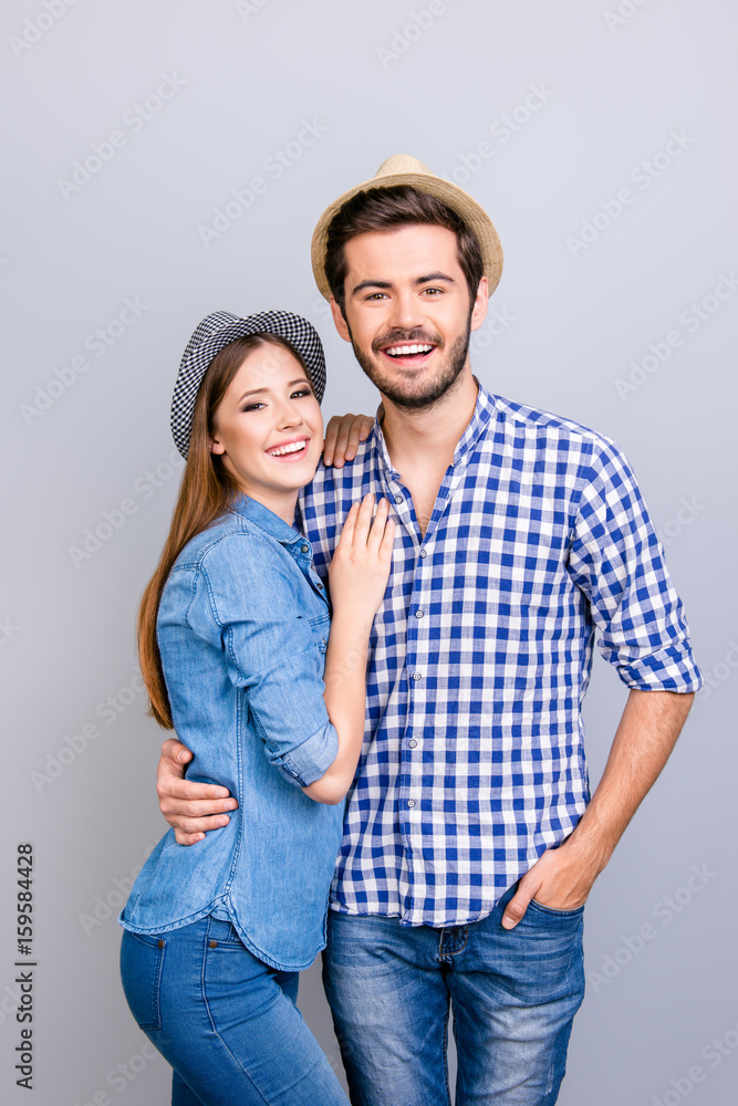 Vacation together. Happy young couple in casual wear and hats are hugging on light background, smiling, posing for a family portrait for memories Vacation together. Happy young couple in casual wear and hats are hugging on light background, smiling, posing for a family portrait for memories