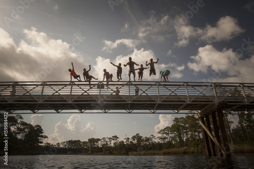 Man and children leaping from footbridge, Miramar Beach, Florida, USA photo