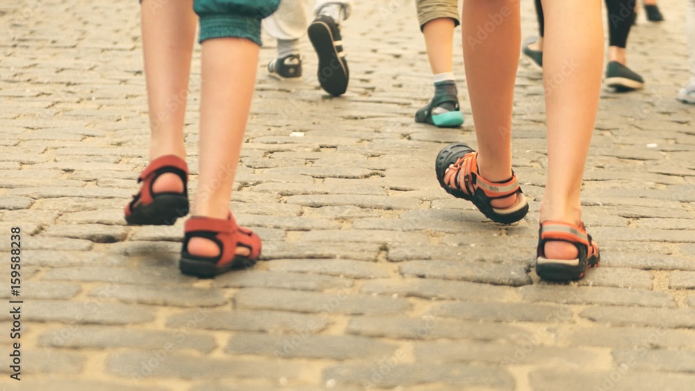 Boys wearing shorts and sandals walk on cobblestone pavement