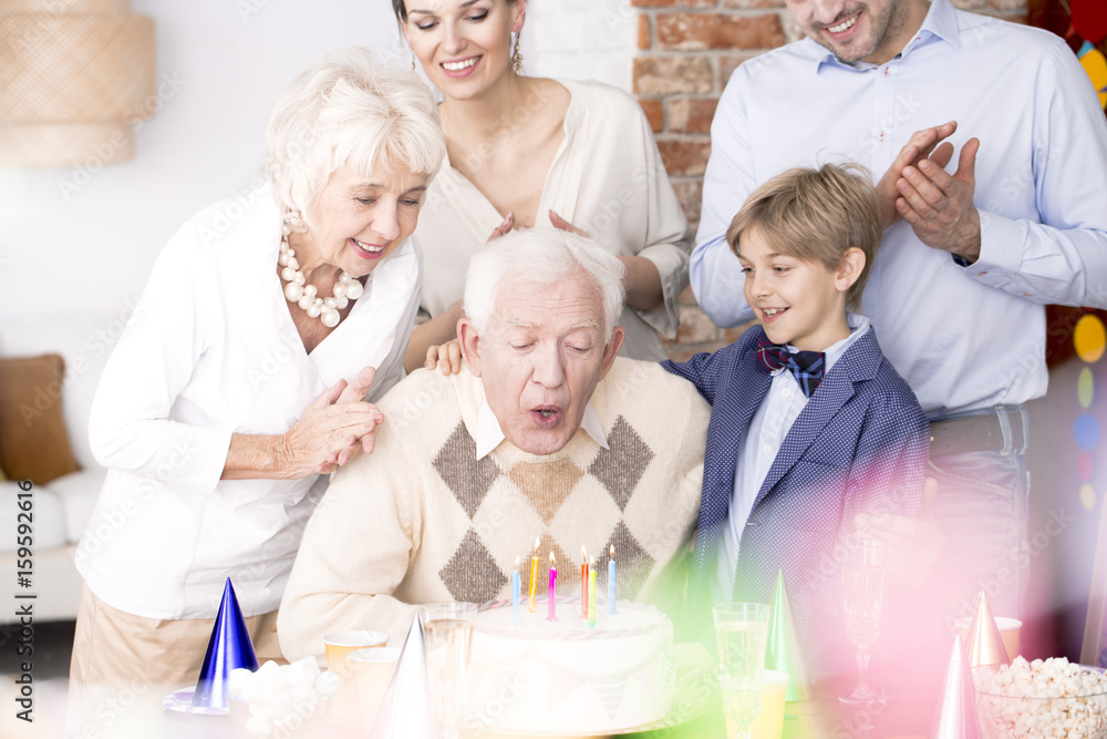 Fototapeta premium Grandpa blowing out candles on birthday cake