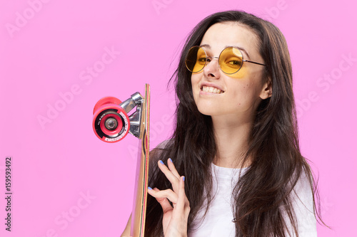 Woman with glasses, woman with skateboard on pink background portrait