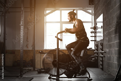 Wallpaper Mural young man using exercise bike at the gym. Fitness male using air bike for cardio workout at crossfit gym. Torontodigital.ca