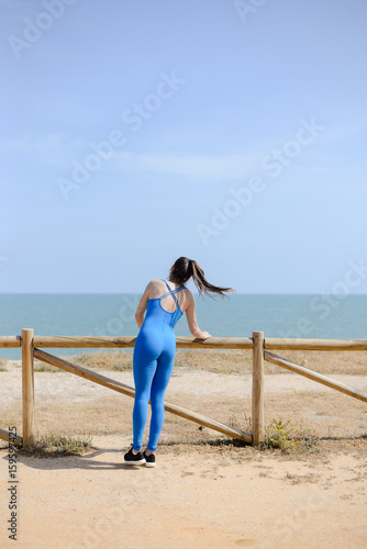 Morning training on the beach. Beautiful female doing workout on sunny blue sky outdoors background. Healthy lifestyle exercises. Back side view of perfect fit shape body © gorosi