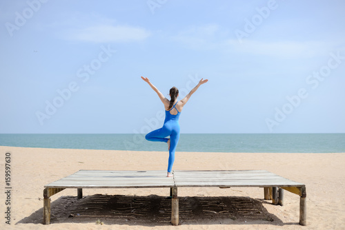 Morning training on the beach. Beautiful female doing workout on sunny blue sky outdoors background. Healthy lifestyle exercises. Back side view of perfect fit shape body