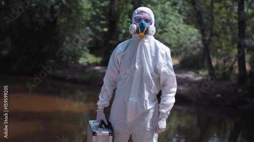 Portrait of anonymous biologist in protective suit holding file and looking at camera on background of nature. photo