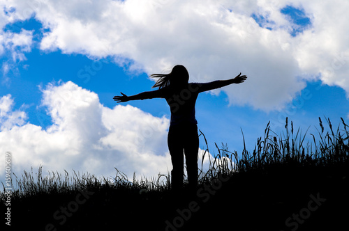 Silhouette young woman open arms on hill