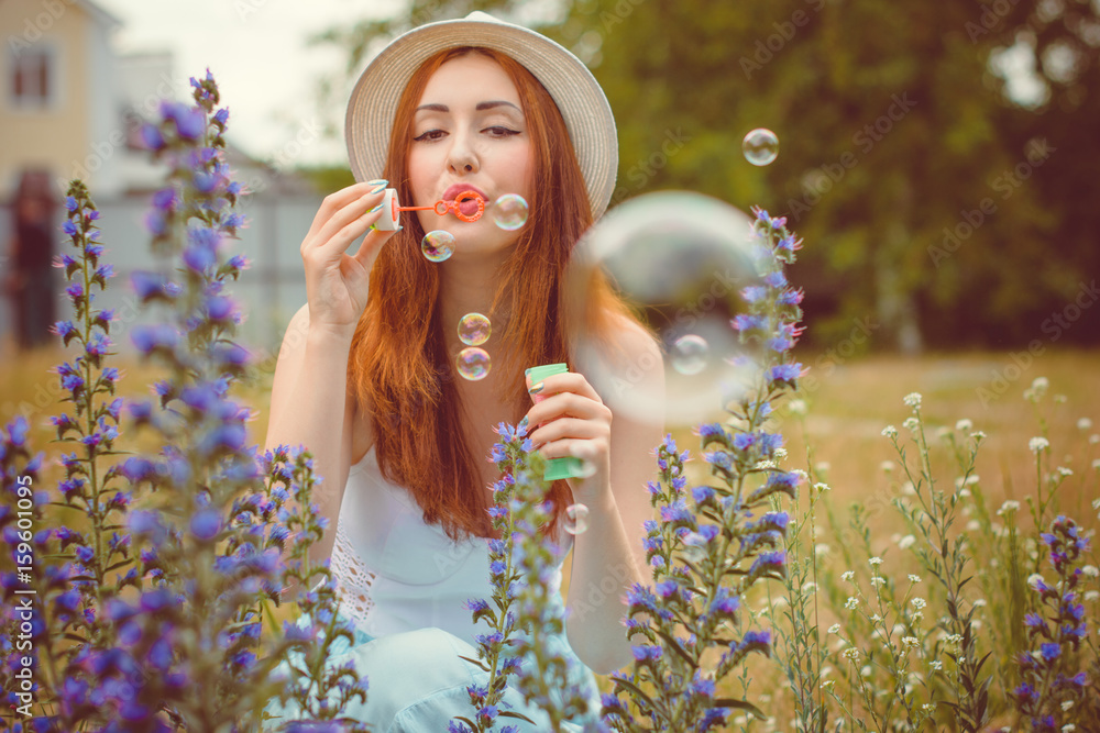 A beautiful Jewish girl in a hat rests on nature surrounded by flowers of trees and herbs enjoys good weather. Summer light and bright style of clothes