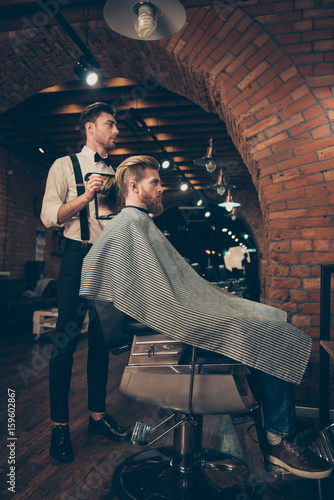 Full length of handsome classy dressed barber shop stylist, who is presenting the result of his styling to a client. Spectacular! Hairdo looks trendy and so perfect