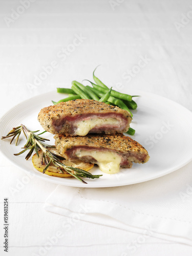 Plate of rose veal cordon bleu, slice of lemon, rosemary and green beans