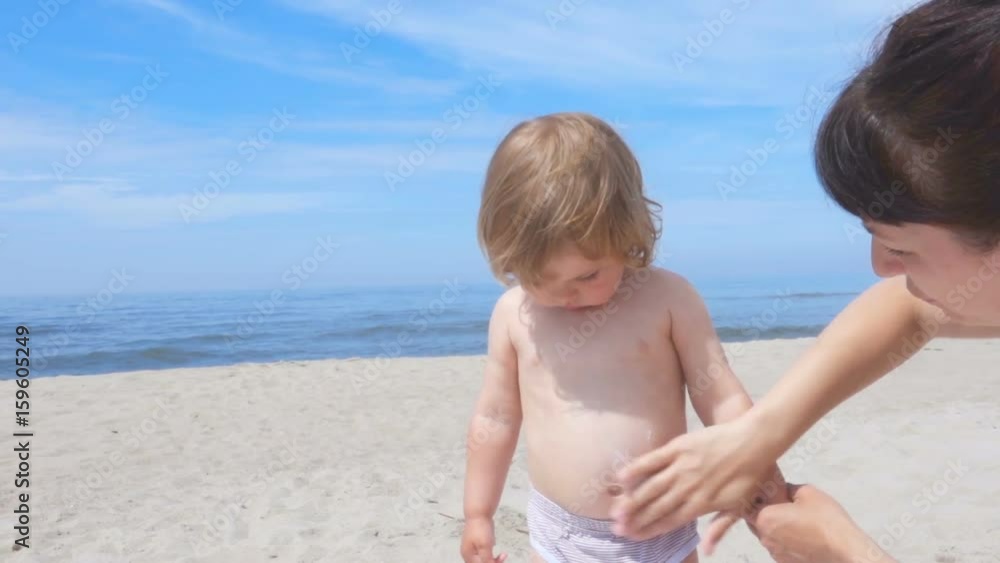 Mother applying sunscreen lotion on son back at beach. Mother preparing child for bath in sea. Mother applying sunscreen lotion on son back at beach. Mother preparing child for bath in sea.