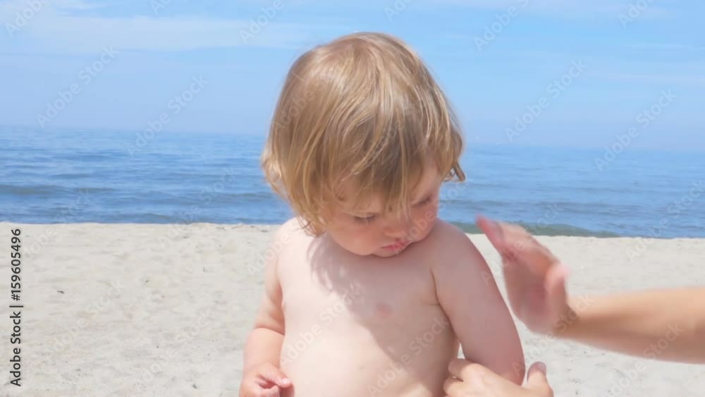 Mother applying sunscreen lotion on son back at beach. Mother preparing child for bath in sea. Mother applying sunscreen lotion on son back at beach. Mother preparing child for bath in sea.