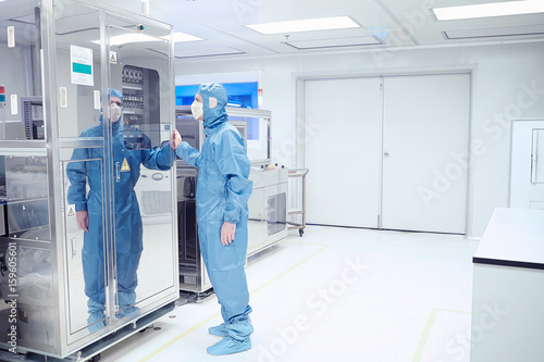 Male worker inspecting manufacturing machinery in flexible electronics factory clean room