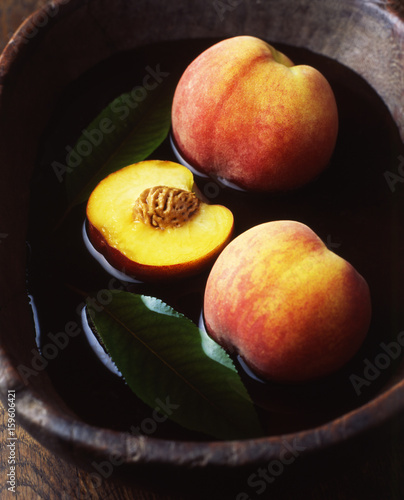 Whole and half peaches and leaves in vintage wooden bowl of water photo