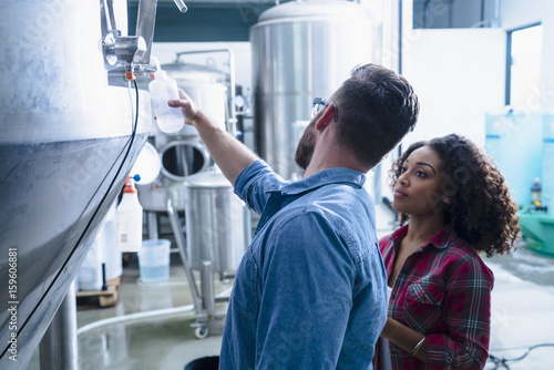 Colleagues in brewery discussing fermentation tank