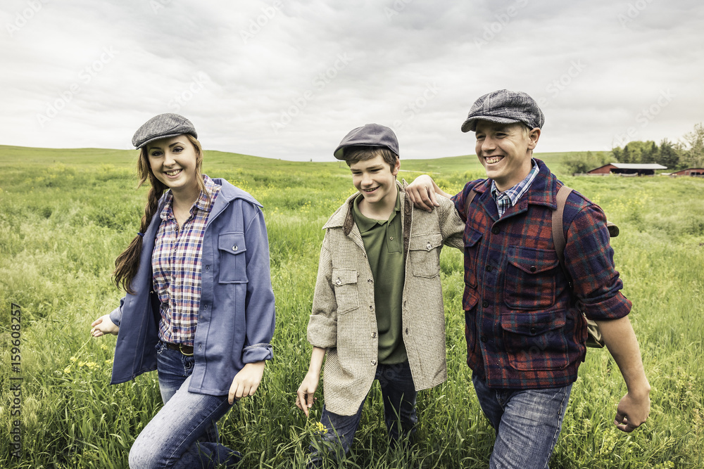 Young adults and teen boy wearing flat caps walking in tall grass looking at camera smiling Young adults and teen boy wearing flat caps walking in tall grass looking at camera smiling