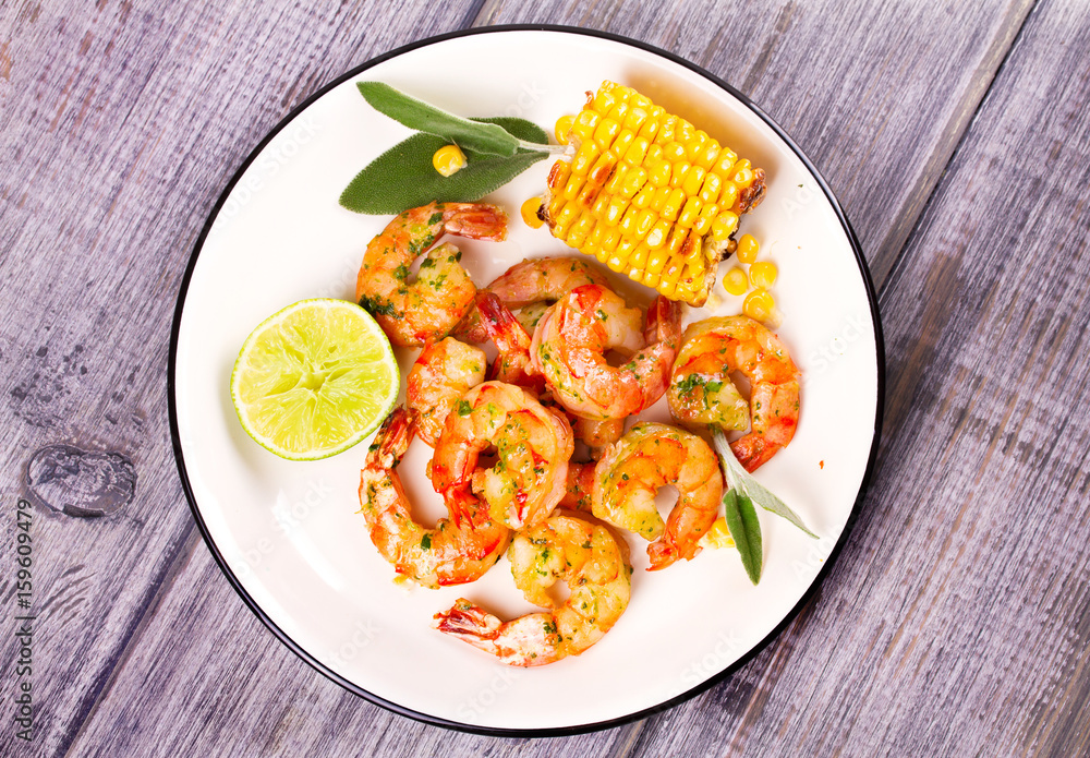 Grilled shrimps and corn garnished with lime and sage leaves. Prawns on white plate. View from above, top studio shot Grilled shrimps and corn garnished with lime and sage leaves. Prawns on white plate. View from above, top studio shot