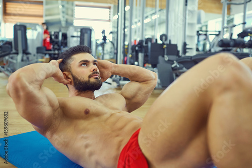 Bodybuilder with a beard does abs exercise on the floor in the gym.