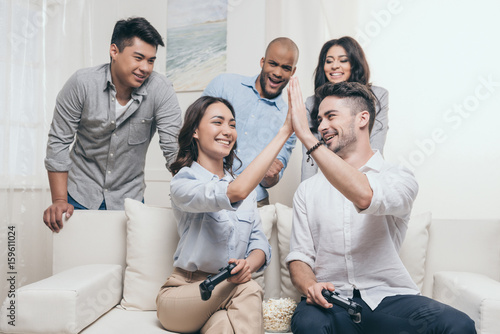 young multiethnic friends playing video games and giving high five at home