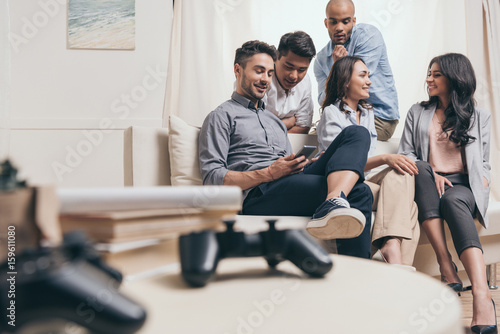 young casual multiethnic friends spending time together while sitting on sofa at home