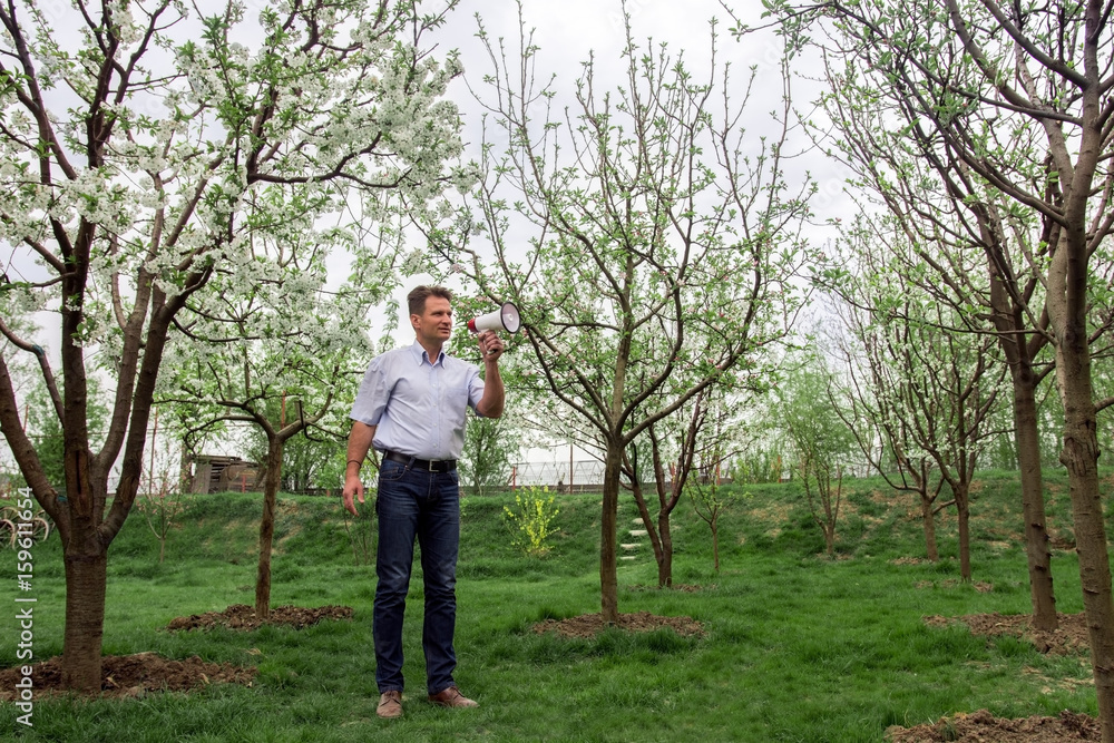 Adult man with megaphone between blooming trees in spring Adult man with megaphone between blooming trees in spring