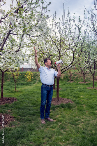 Adult man with megaphone between fruit trees in spring