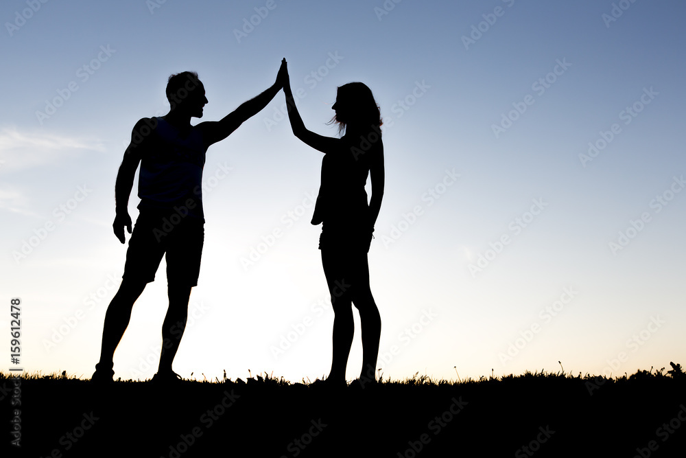 Happy silhouette couple holding up hands against the sky at dusk