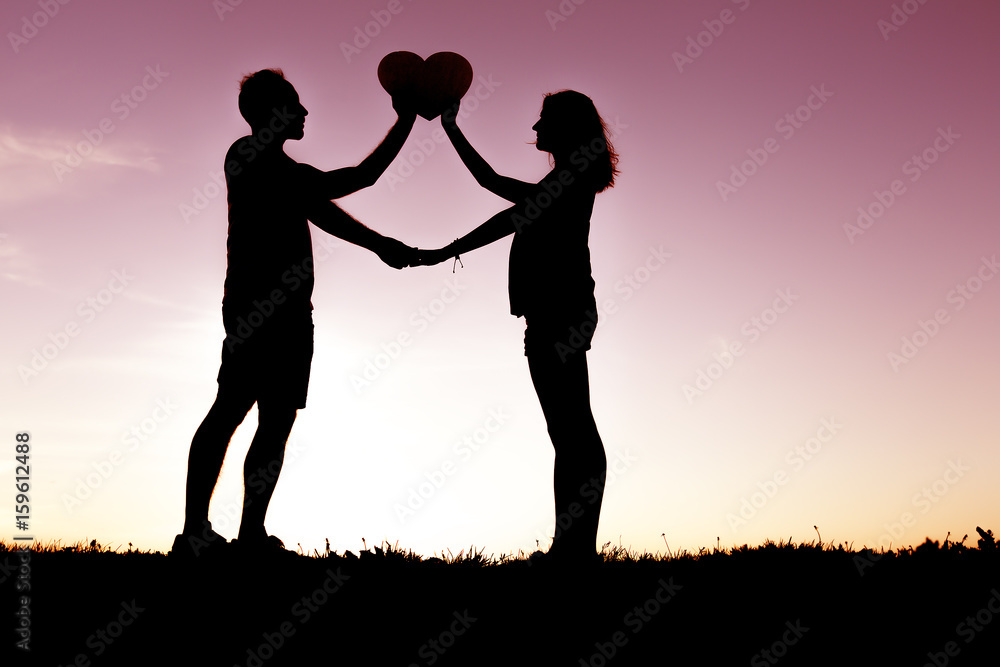 Romantic young couple holding heart shape on hands at sunset Romantic young couple holding heart shape on hands at sunset