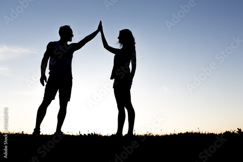 Happy silhouette couple holding up hands against the sky at dusk