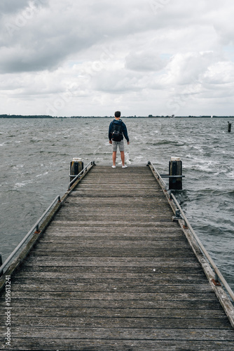 Back view of boy with casual clothing on wooden pier a cloudy summer day. Concept freedom