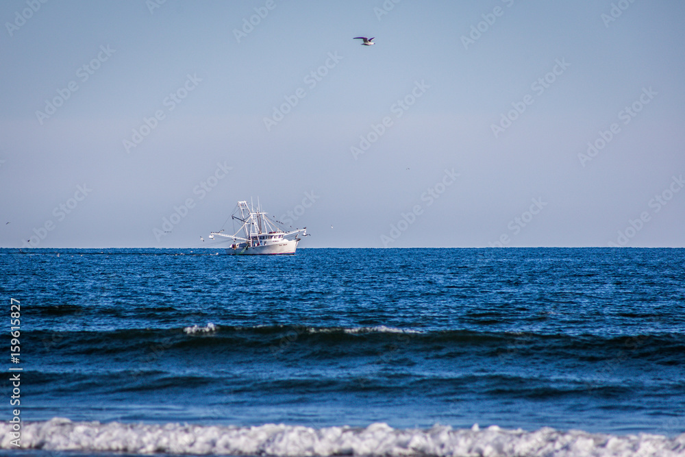 Shrimp boat on the open calm sea with a bird flying overhead