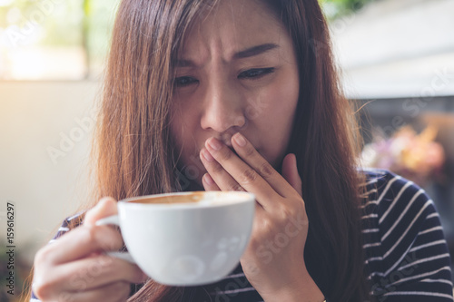 Bilde på lerret Closeup image of Asian woman holding hot coffee with feeling strange and smellin
