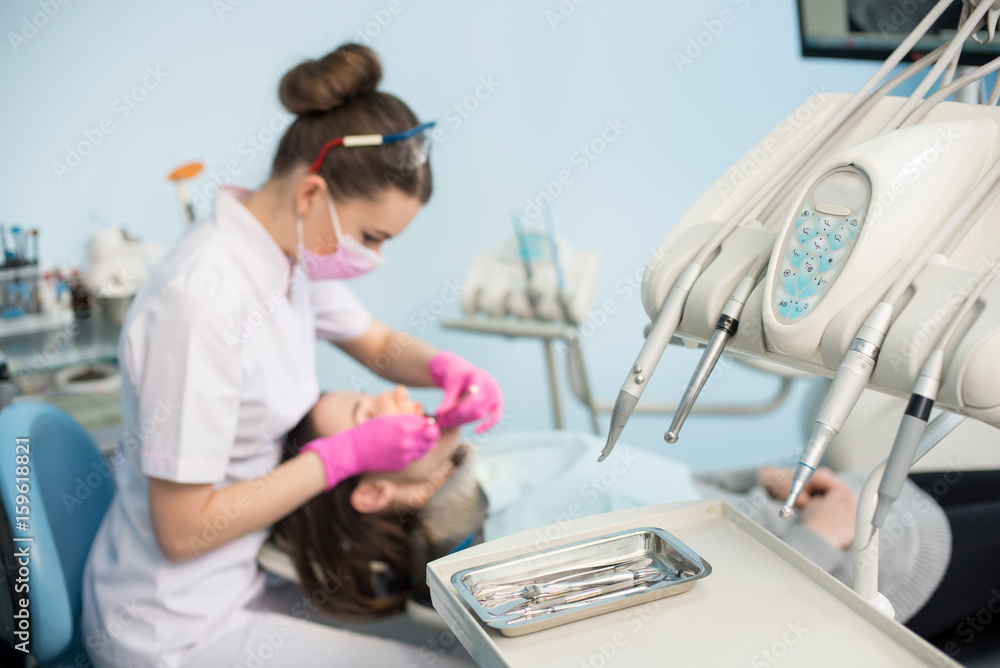 Professional dental instruments for first check-up, on the blurred background dentist is treating patient in dental clinic. Selective focus. Stomatology Professional dental instruments for first check-up, on the blurred background dentist is treating patient in dental clinic. Selective focus. Stomatology