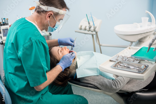 Male dentist with dental tools - mirror and probe treating patient teeth at dental clinic office. Medicine, dentistry and health care concept. Dental equipment