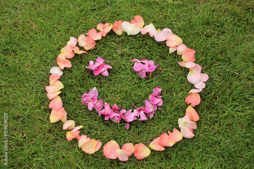 Smiley face emoticon from petals of rose on background of grass. Copy space is left and bottom.
