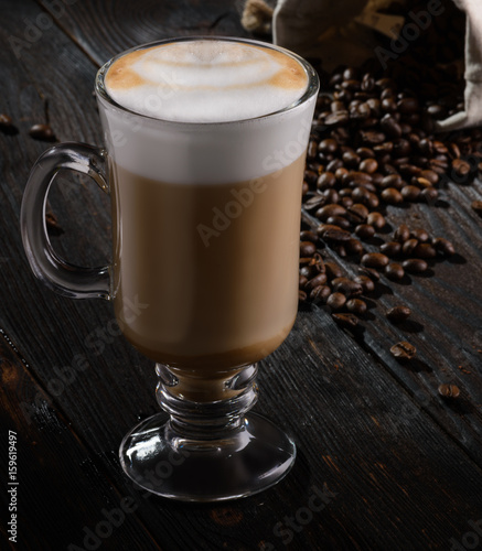 Irish coffee with cappuccino foam on dark wooden background with coffee beans