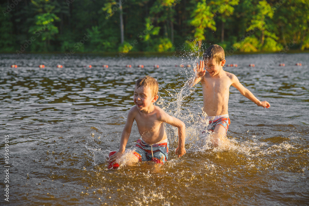 Laughing children splashing in the lake. Two boys having fun and playing in water outdoors. Summer vacation concept Laughing children splashing in the lake. Two boys having fun and playing in water outdoors. Summer vacation concept