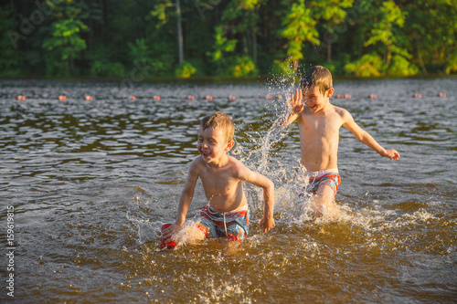 Fototapeta Naklejka Na Ścianę i Meble -  Laughing children splashing in the lake. Two boys having fun and playing in water outdoors. Summer vacation concept