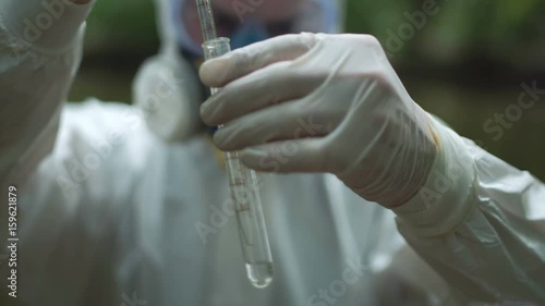 Anonymous ecologist in protective suit holding glass test tube.