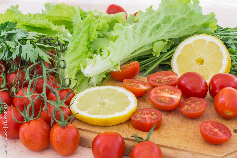 Cherry tomatoes, lemon plastics, parsley and lettuce leaves covered with drops of water lie on the kitchen table Cherry tomatoes, lemon plastics, parsley and lettuce leaves covered with drops of water lie on the kitchen table