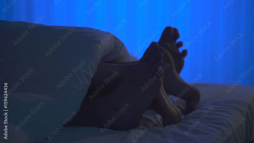The feet under a cover on the bed. night time The feet under a cover on the bed. night time