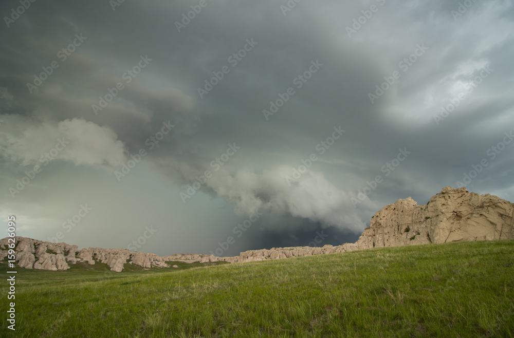 A shelf cloud accompanies this thunderstorm as it approaches a rocky hillside in the Great Plains.
