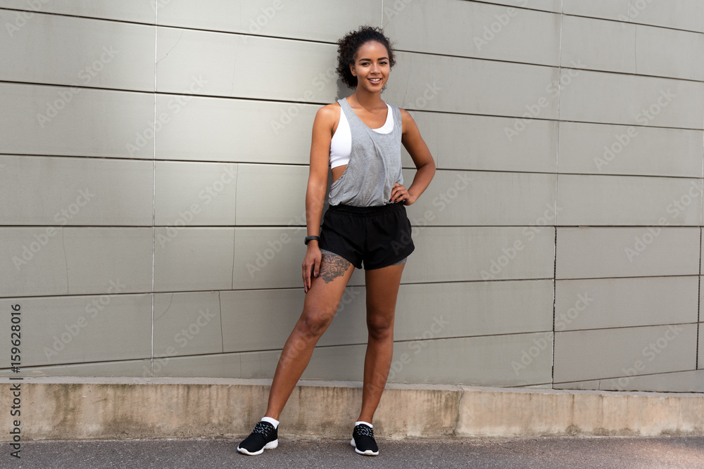 Fototapeta premium Portrait of young female athlete standing outdoors at wall