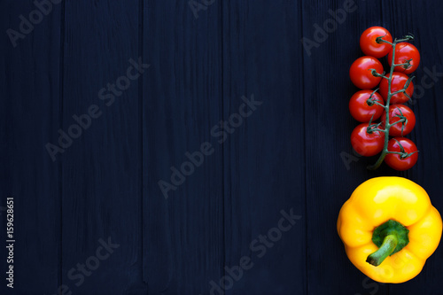 Cherry tomatoes and yellow bell pepper on black rustic wooden background, free space for advertising or text