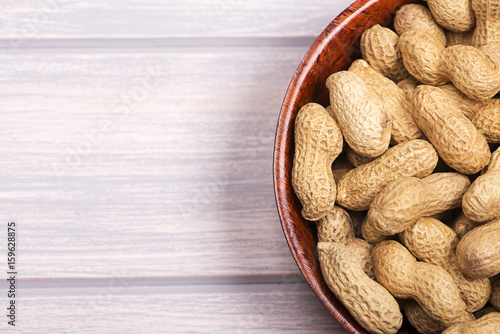 From above pile of whole peanuts in bowl on white wooden background. Copy space.