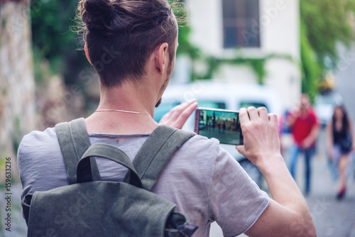 Man backpack makes a photo on your smartphone on a city street photo