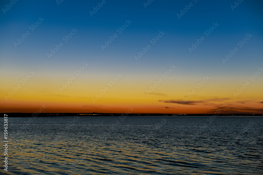 Fototapeta premium Sunset over the lake with the lights of a small town in the distance