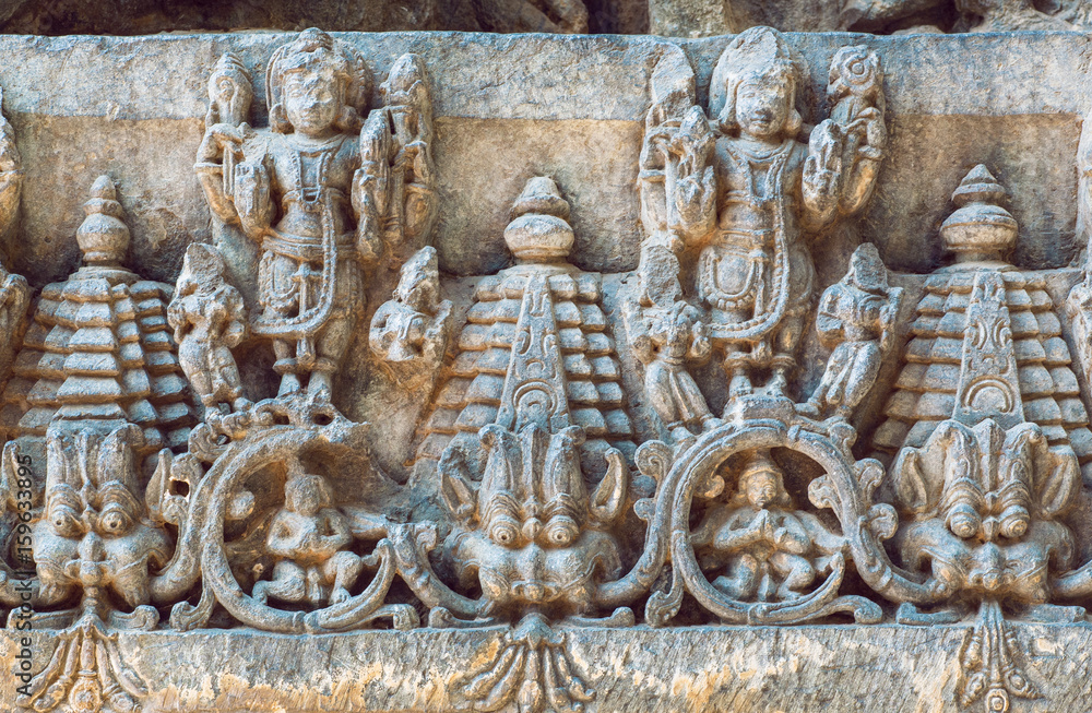 Old Indian architecture background on traditional style relief, with fantasy animals, ancient people and patterns inside the 12th century Hoysaleshwara temple in Halebidu, India.