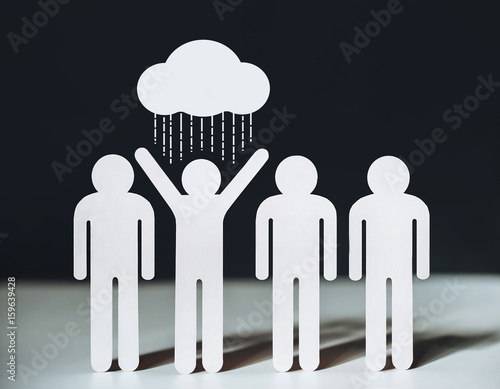     A group of people with a person who expresses the idea of inappropriate optimism. Concept. Cloud and rain, which is spilled on the unfortunate merry man. Cut people out of paper. 