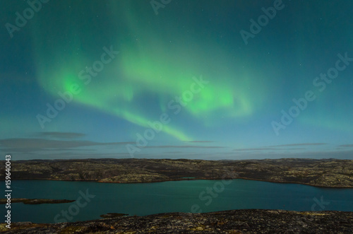 The Aurora in the sky above the hills and water on a moonlit night. © Moroshka